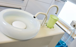 Ein weißes Waschbecken mit zwei Wasserhähnen und einem grünen Becher daneben.